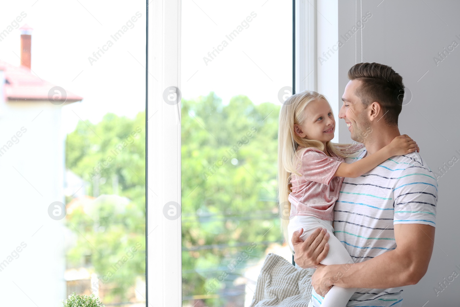 Photo of Young man with cute little girl near window at home