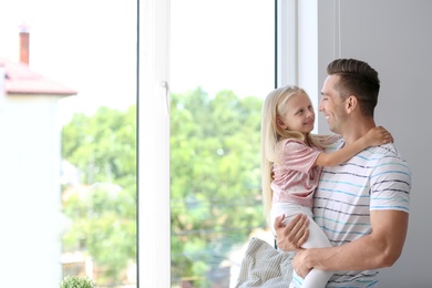 Photo of Young man with cute little girl near window at home