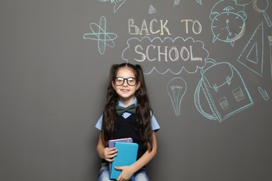 Photo of Little child in uniform near drawings with text BACK TO SCHOOL on grey background