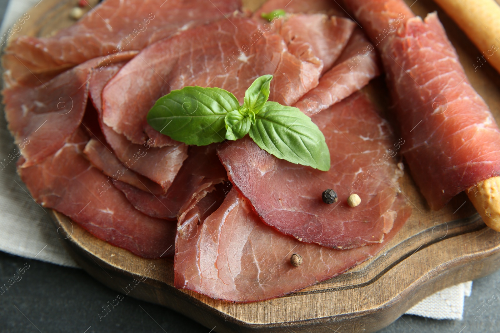 Photo of Delicious bresaola and basil leaves on grey table, closeup