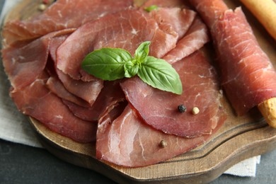 Delicious bresaola and basil leaves on grey table, closeup