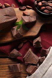 Photo of Pieces of tasty milk chocolate and cocoa beans on wooden table, flat lay