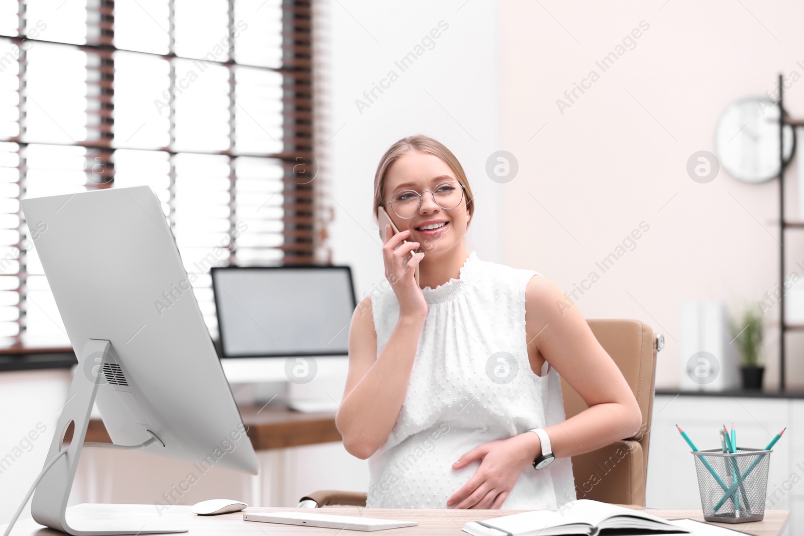 Photo of Young pregnant woman talking on phone while working in office