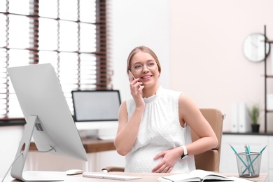 Young pregnant woman talking on phone while working in office