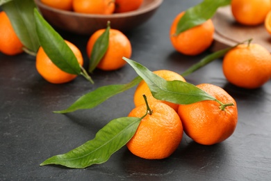 Photo of Fresh tangerines with green leaves on black table