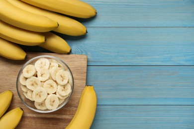 Photo of Bowl with cut bananas near whole fruits on light blue wooden table, flat lay. Space for text