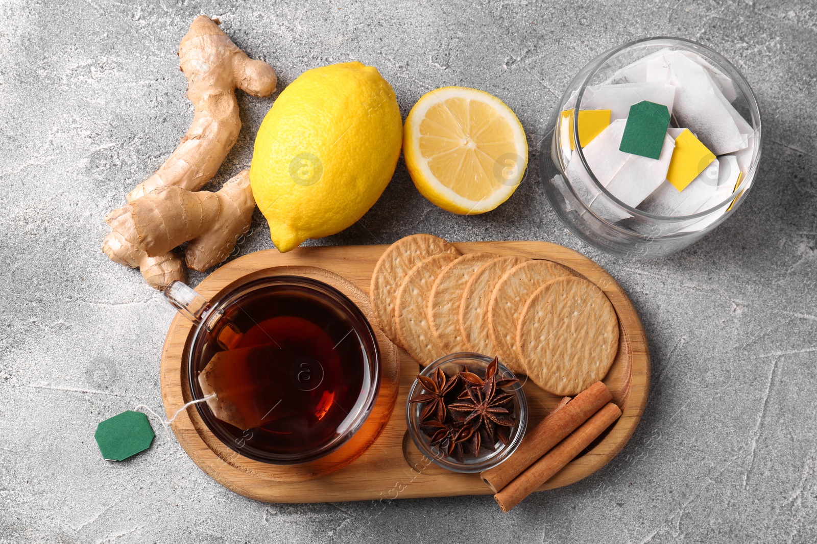 Photo of Tea bags, cup of hot drink, cookies and ingredients on light grey table, flat lay