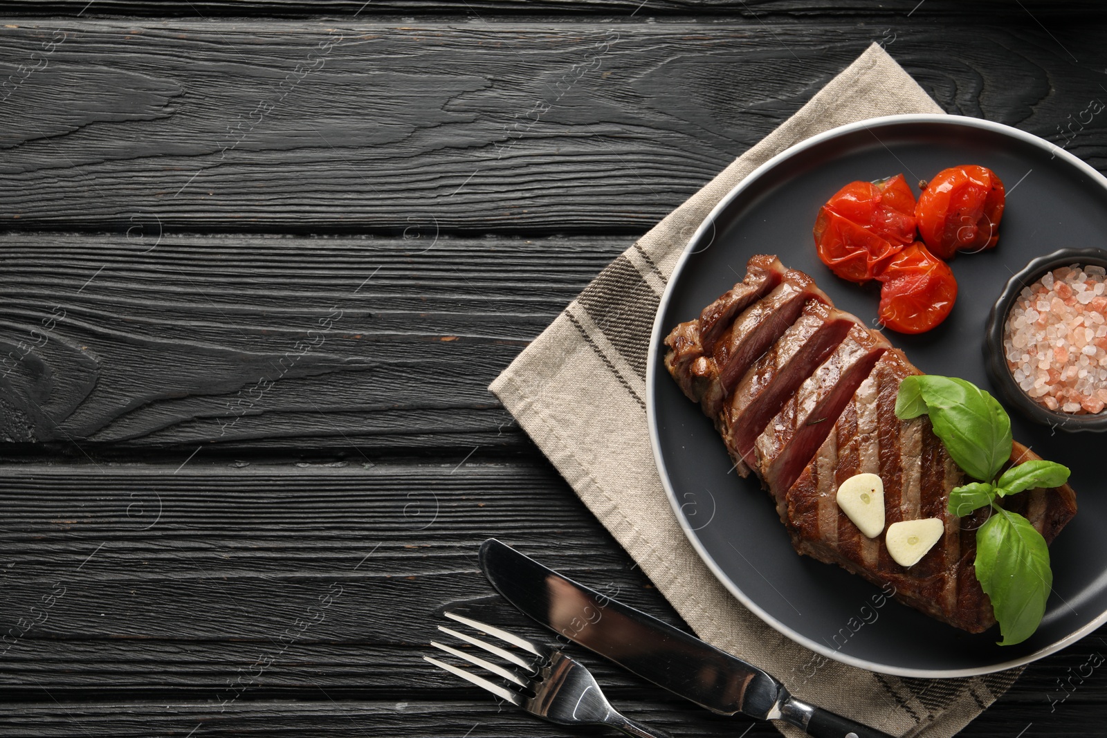 Photo of Delicious grilled beef steak served with spices and tomatoes on black wooden table, flat lay. Space for text