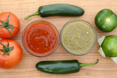 Photo of Tasty salsa sauces, jalapeno peppers and different tomatoes on wooden table, flat lay