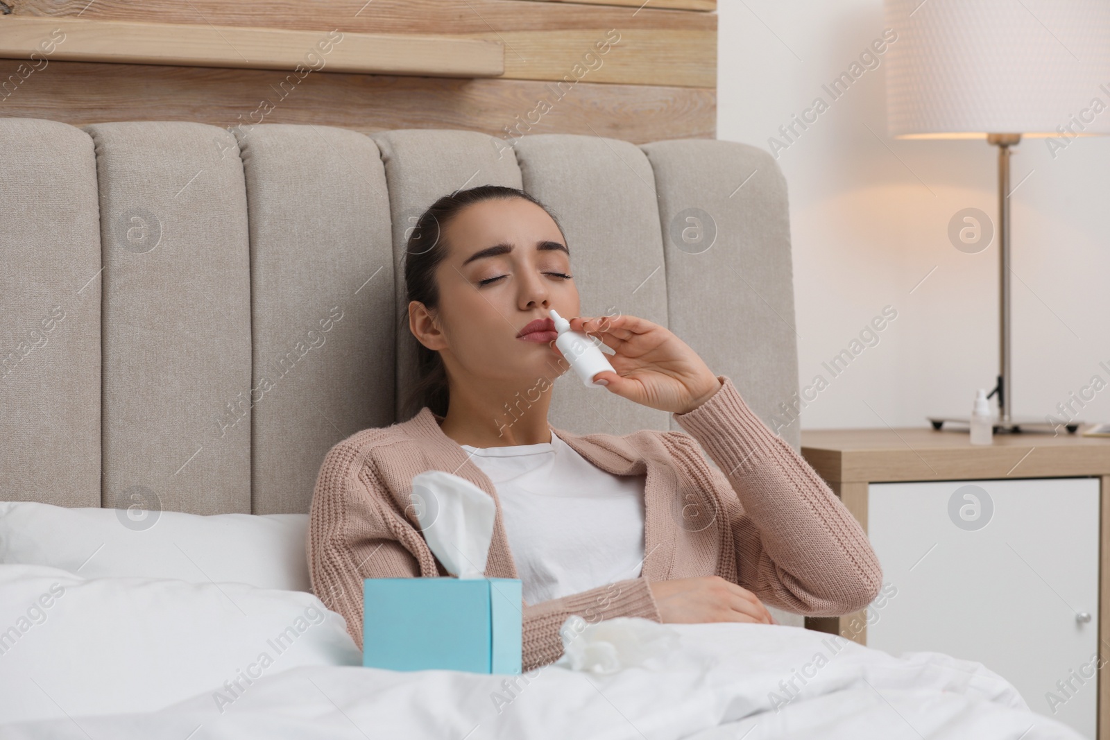 Photo of Sick young woman using nasal spray in bed at home