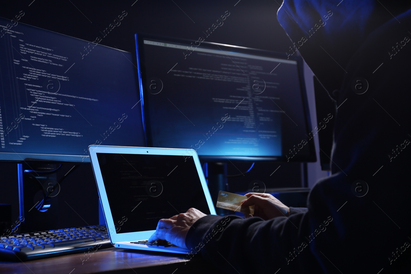 Photo of Hacker with computers and credit card in dark room, closeup. Cyber crime