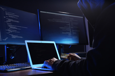 Photo of Hacker with computers and credit card in dark room, closeup. Cyber crime