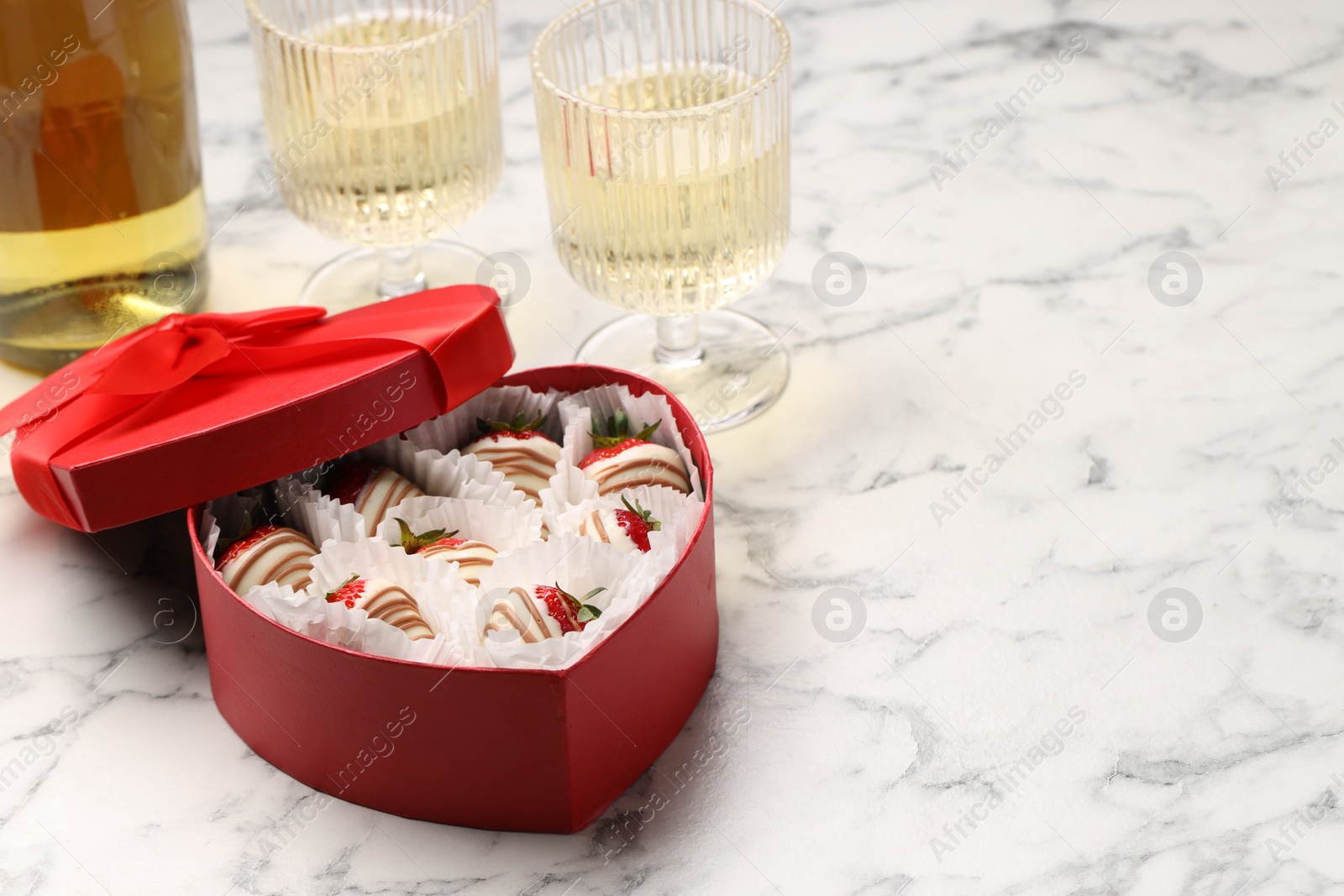 Photo of Delicious chocolate covered strawberries in heart shaped box and sparkling wine on white marble table. Space for text