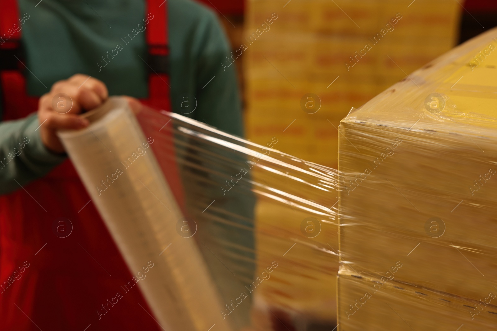 Photo of Worker wrapping boxes in stretch film at warehouse, closeup