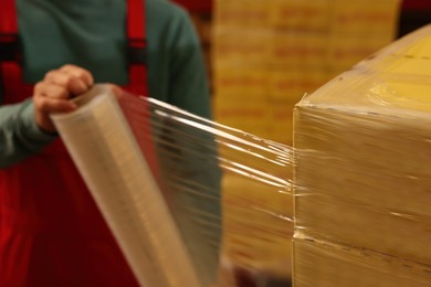 Photo of Worker wrapping boxes in stretch film at warehouse, closeup