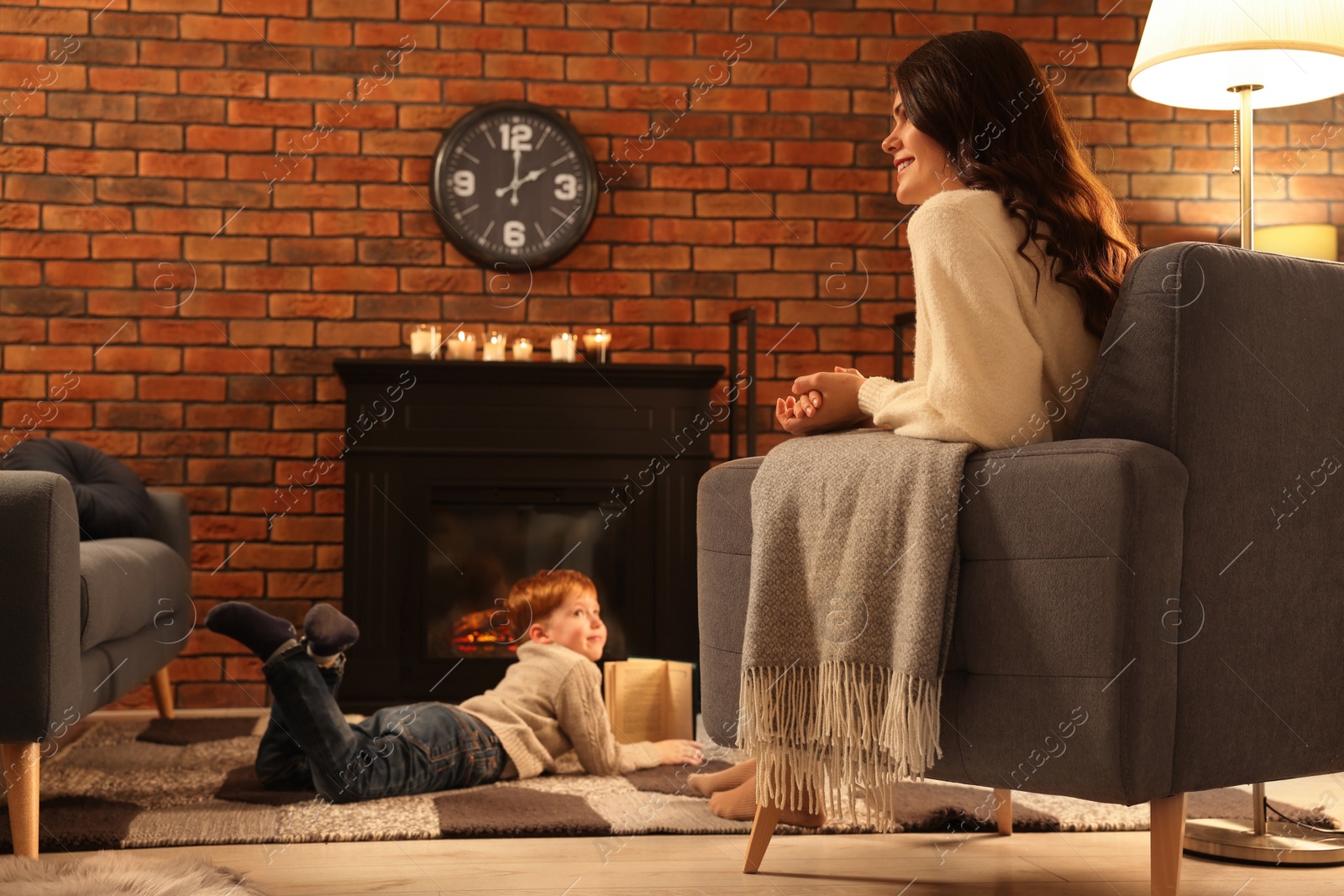 Photo of Happy mother and son spending time near fireplace at home