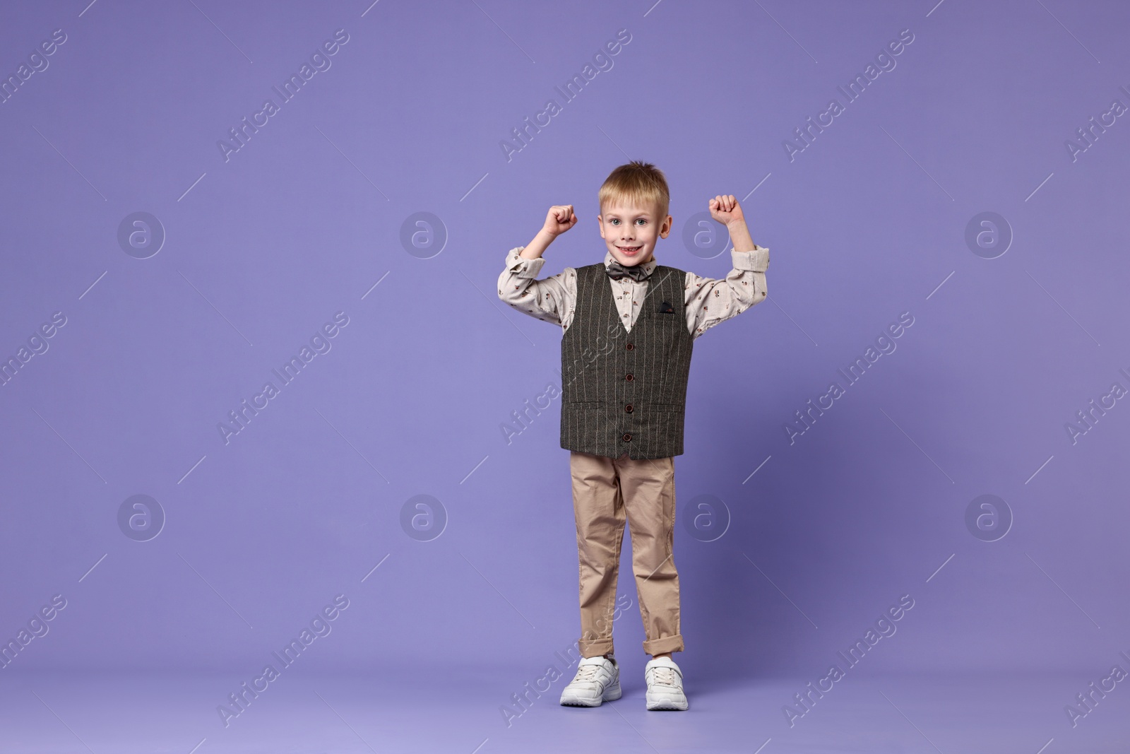 Photo of Happy little boy dancing on violet background. Space for text