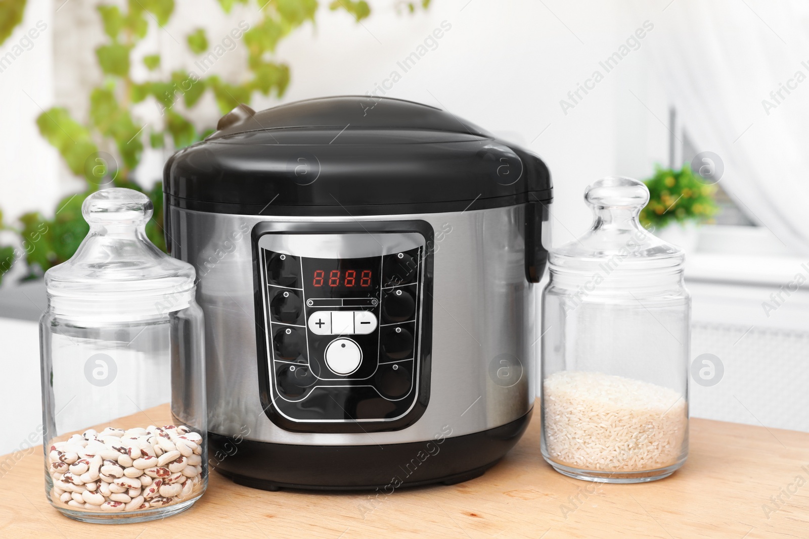 Photo of Jars with rice and beans near modern multi cooker on table in kitchen