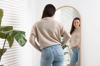 Young woman in stylish jeans near mirror indoors