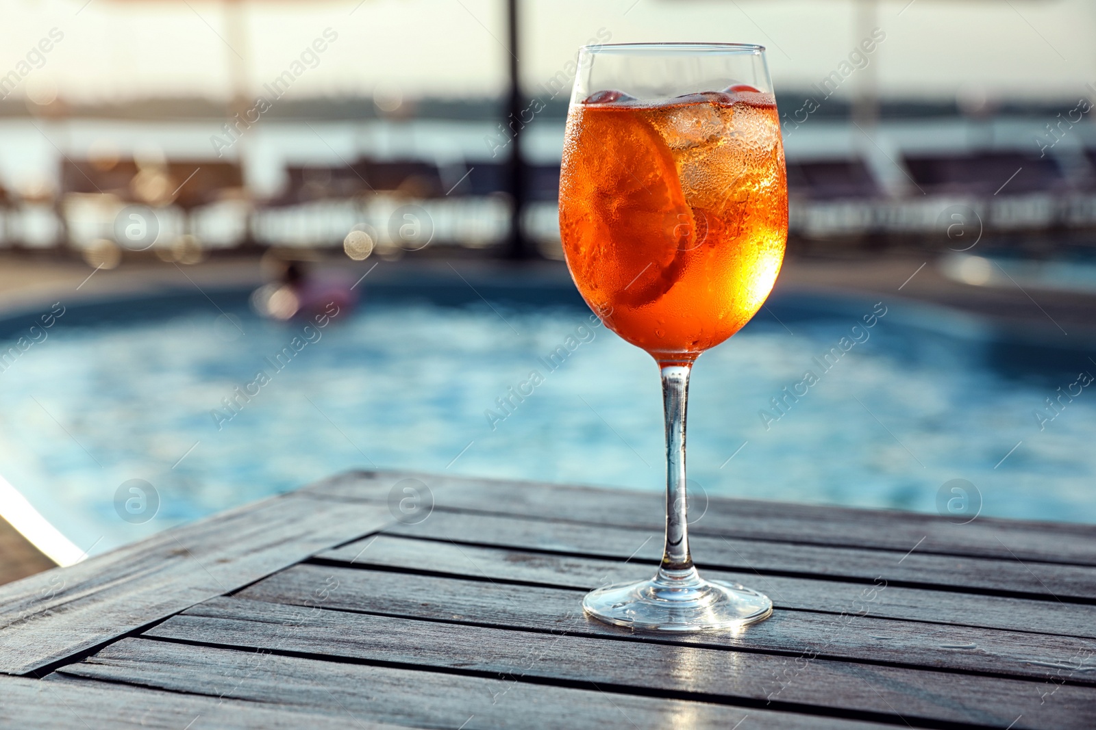 Photo of Glass of fresh summer cocktail on wooden table near swimming pool outdoors. Space for text