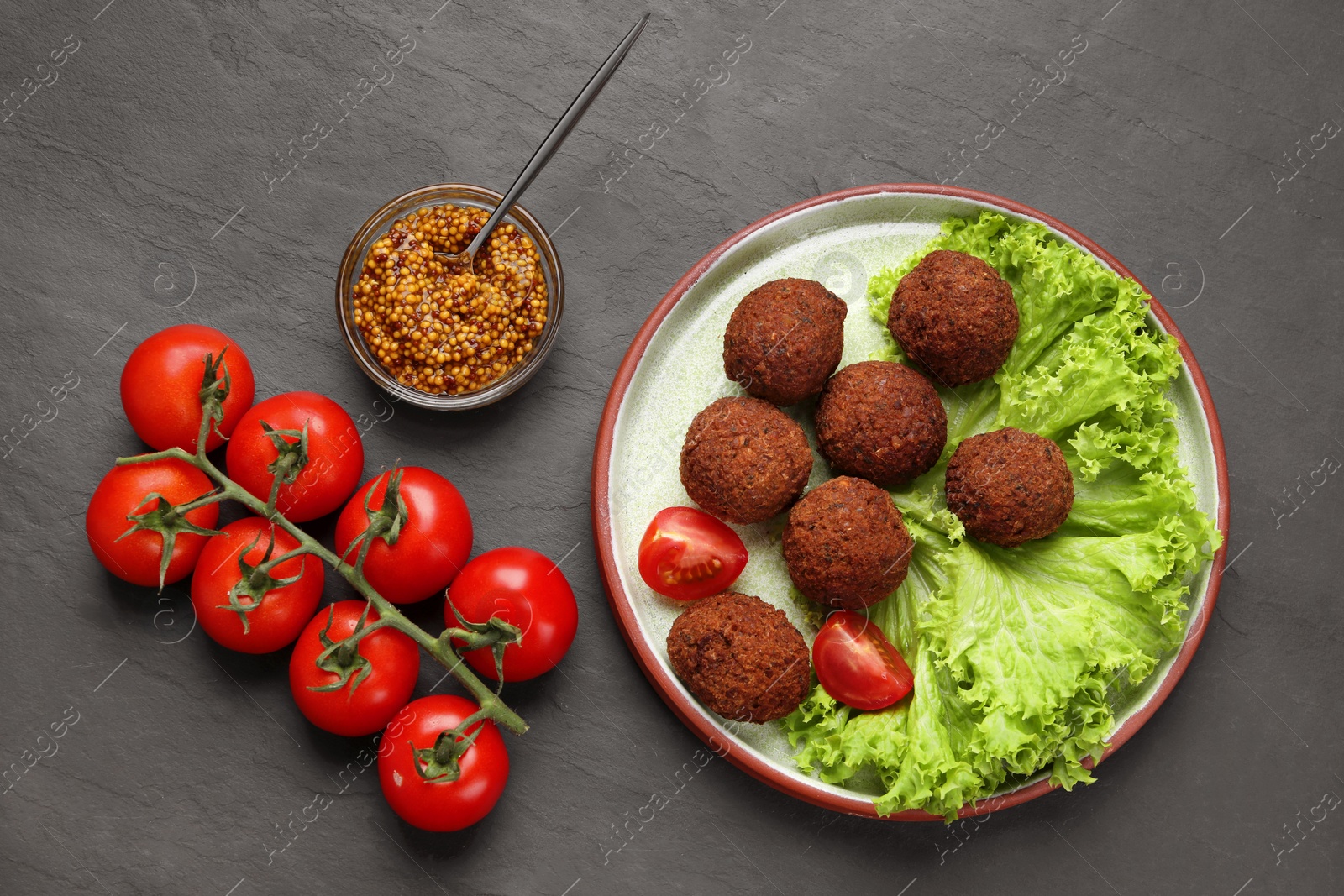 Photo of Delicious falafel balls, tomatoes, lettuce and grain mustard on dark grey textured table, flat lay. Vegan meat products