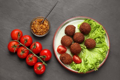 Photo of Delicious falafel balls, tomatoes, lettuce and grain mustard on dark grey textured table, flat lay. Vegan meat products