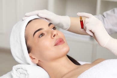 Photo of Professional cosmetologist holding skincare ampoule while working with client in clinic, closeup