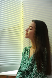 Photo of Young woman near window with Venetian blinds