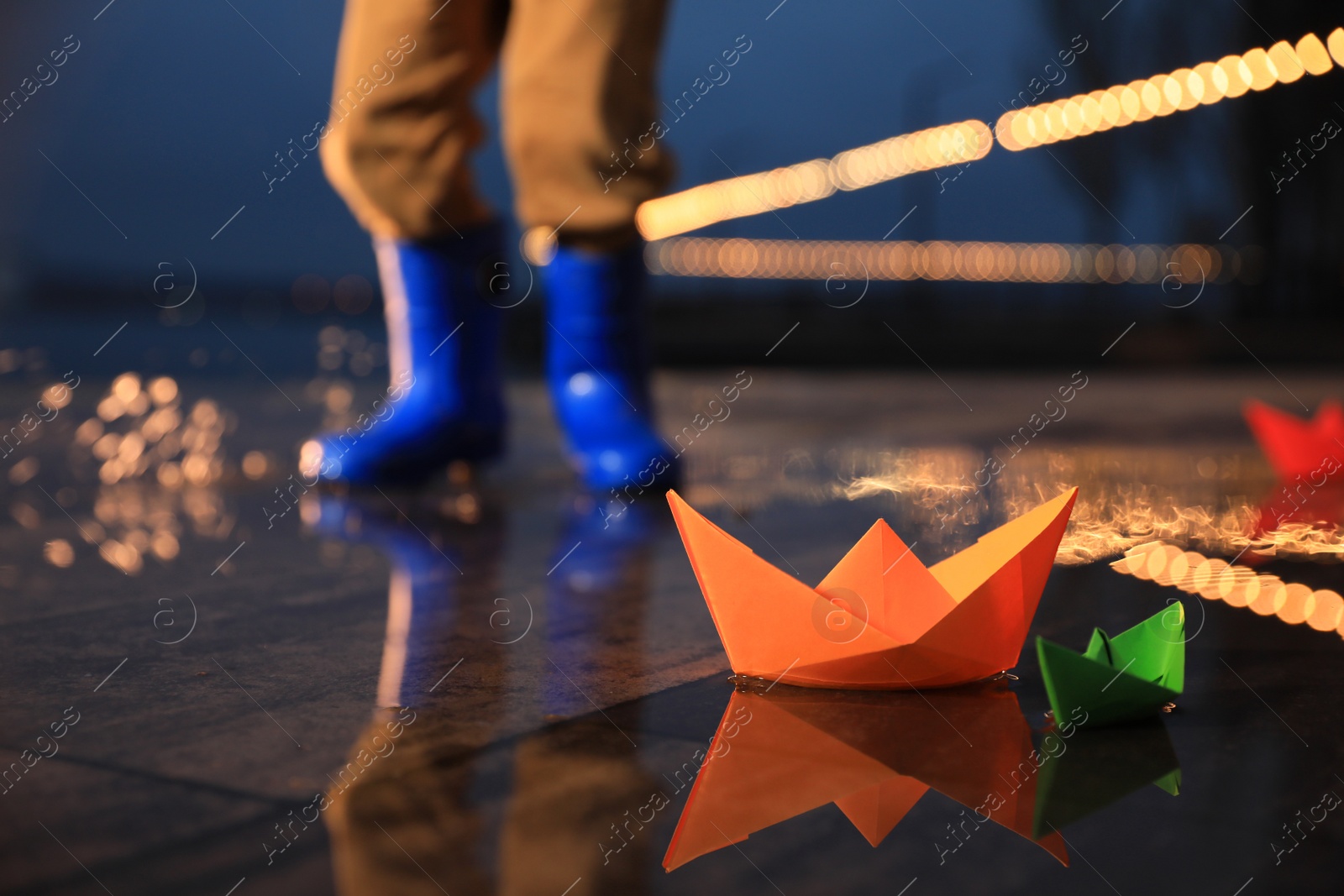 Photo of Little boy outdoors, focus on paper boats in puddle