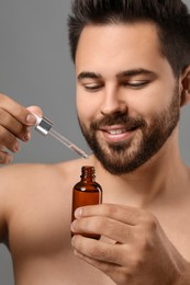 Photo of Handsome man with cosmetic serum in hands on grey background