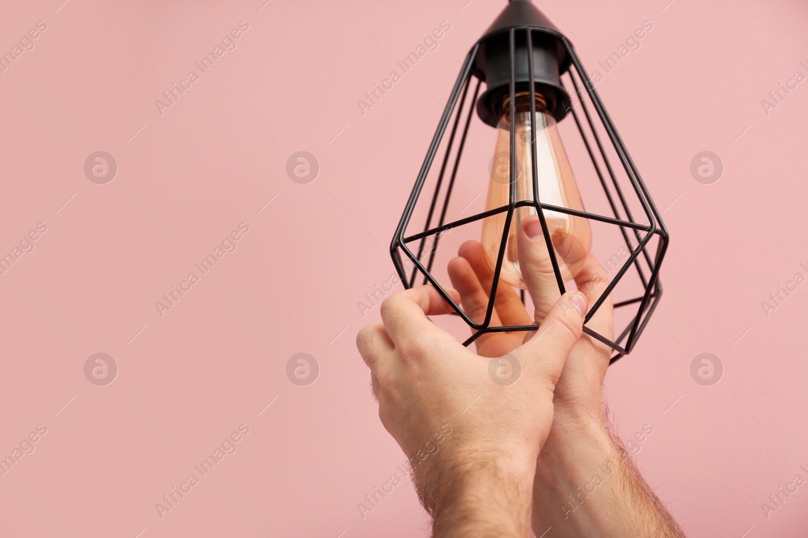 Photo of Man changing light bulb in lamp on color background. Space for text