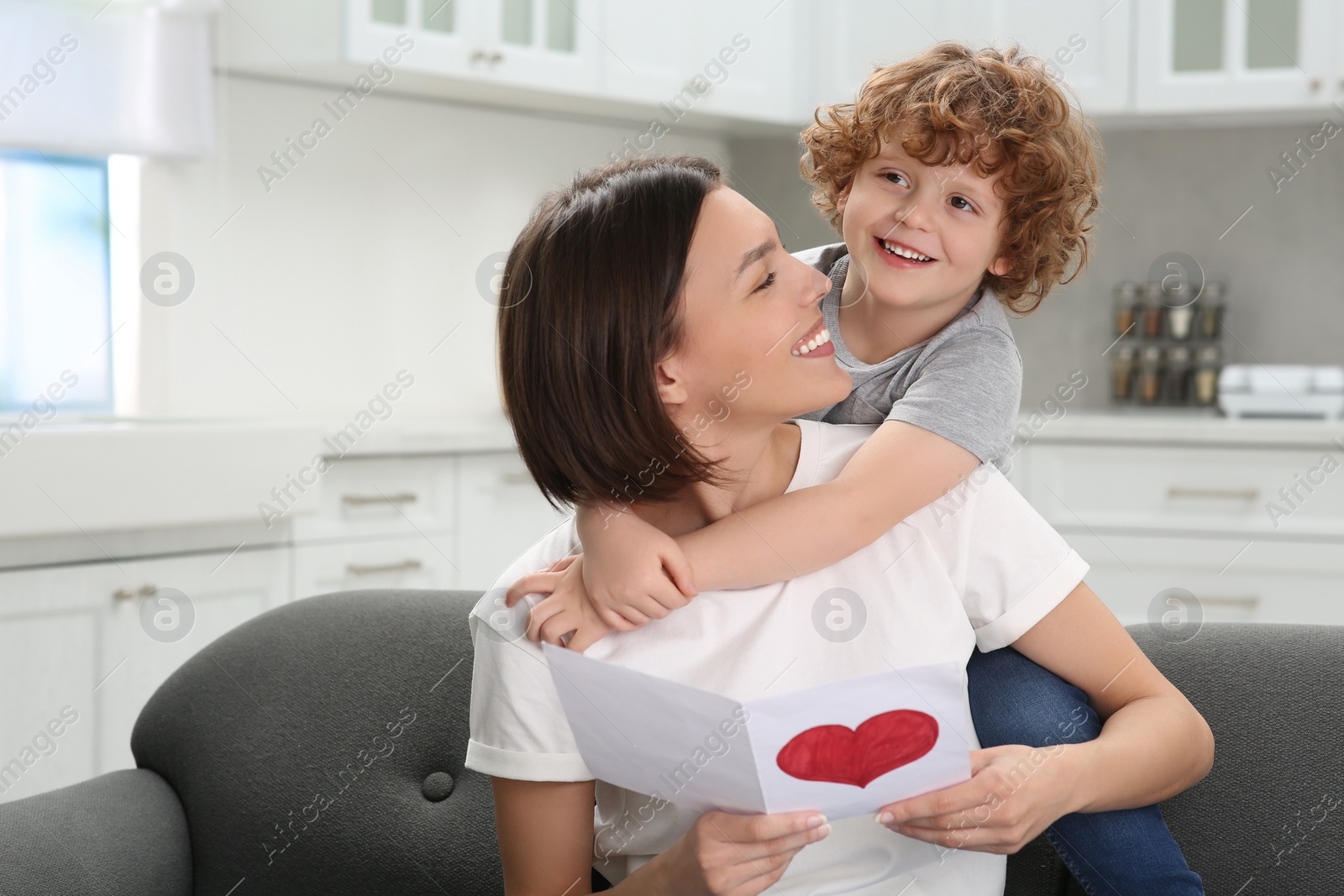 Photo of Little son congratulating his mom with Mother`s day at home. Woman holding greeting card