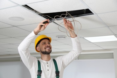 Photo of Electrician with pliers repairing ceiling wiring indoors