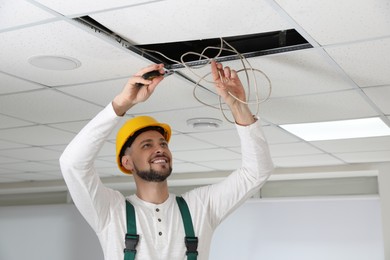 Electrician with pliers repairing ceiling wiring indoors