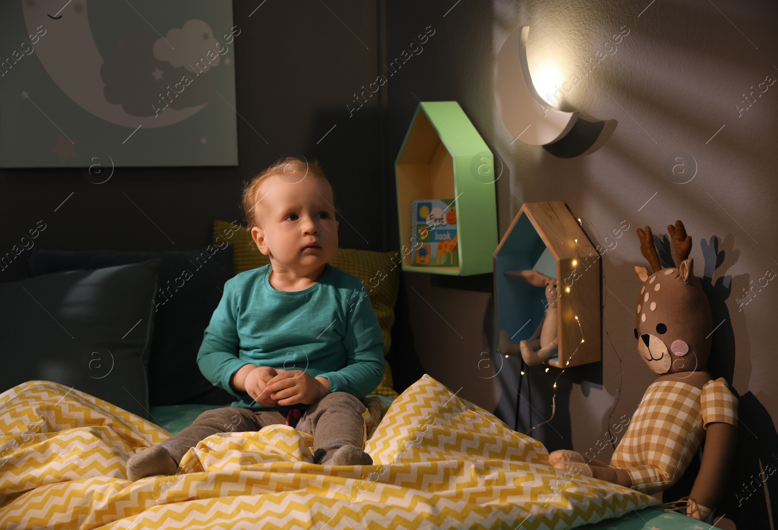 Photo of Cute child in room with crescent shaped night lamp