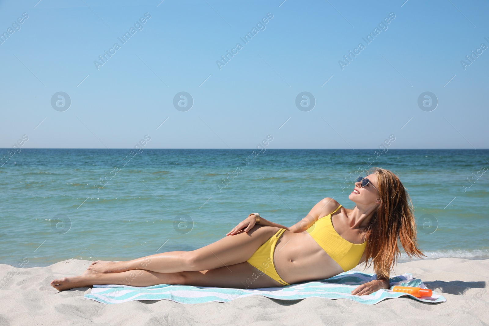 Photo of Beautiful woman with beach towel and sunscreen on sand near sea