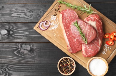 Photo of Pieces of raw beef meat and spices on black wooden table, top view. Space for text