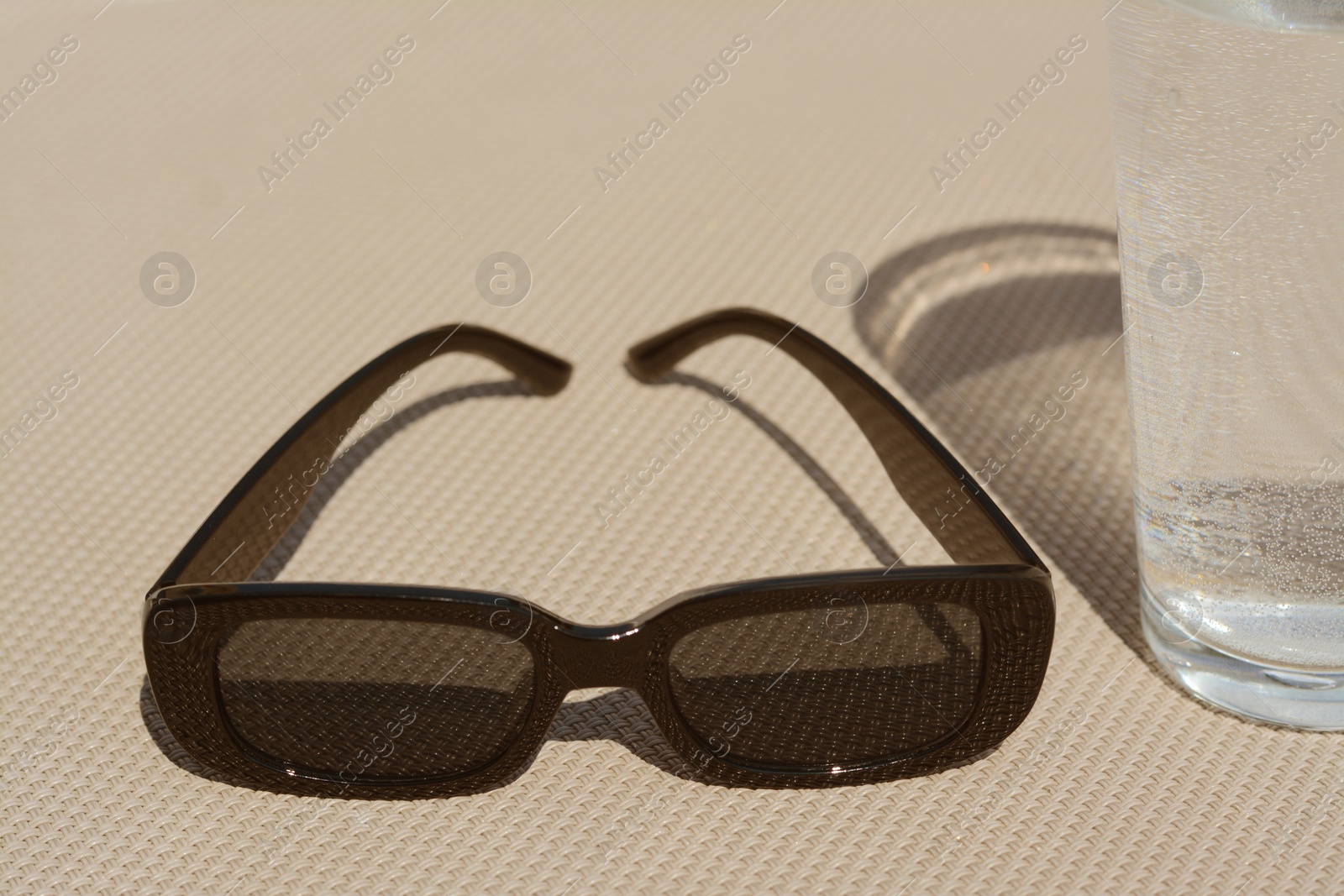 Photo of Stylish sunglasses and glass of water on grey surface, closeup