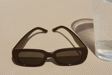 Stylish sunglasses and glass of water on grey surface, closeup