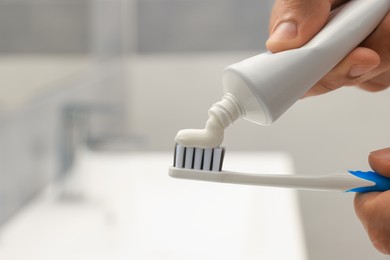 Man applying toothpaste on brush in bathroom, closeup. Space for text