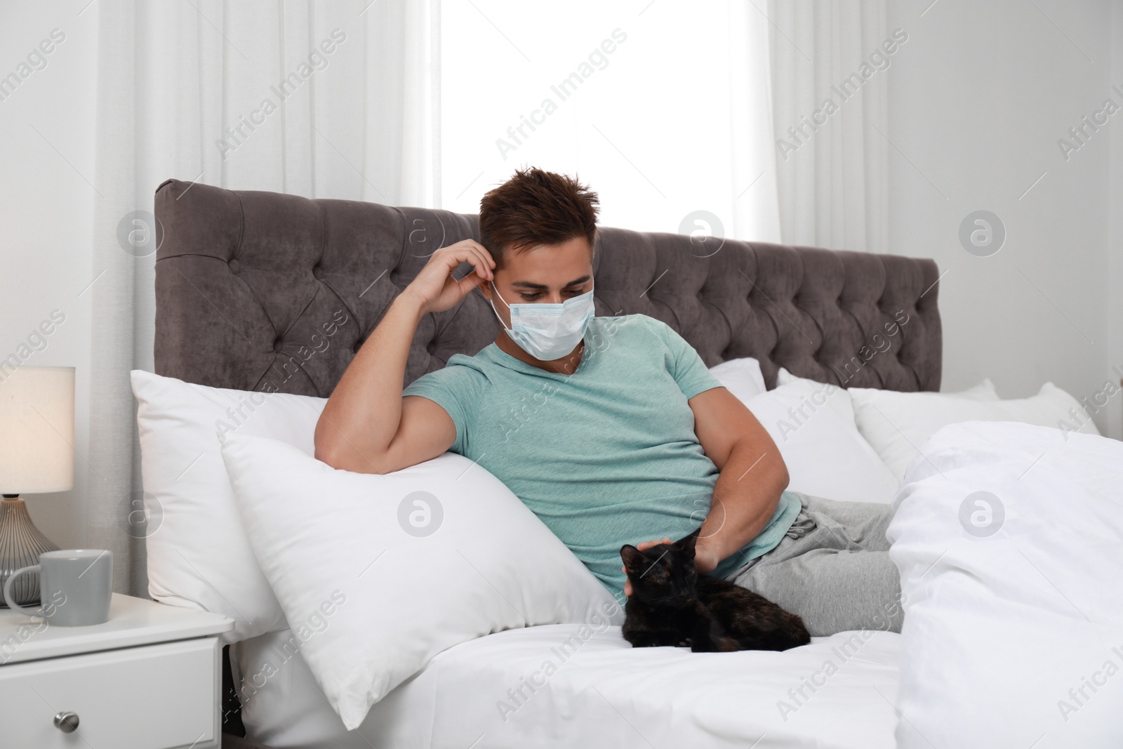 Photo of Young man with cat suffering from allergy in bedroom