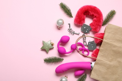 Paper bag with different sex toys and Christmas balls on pink background, flat lay