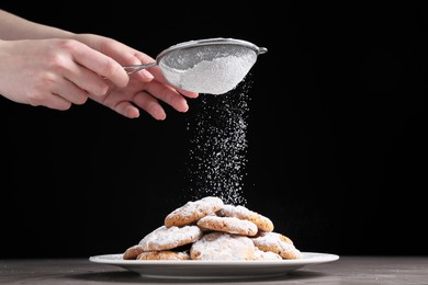 Photo of Woman with sieve sprinkling powdered sugar onto cookies at grey table, closeup