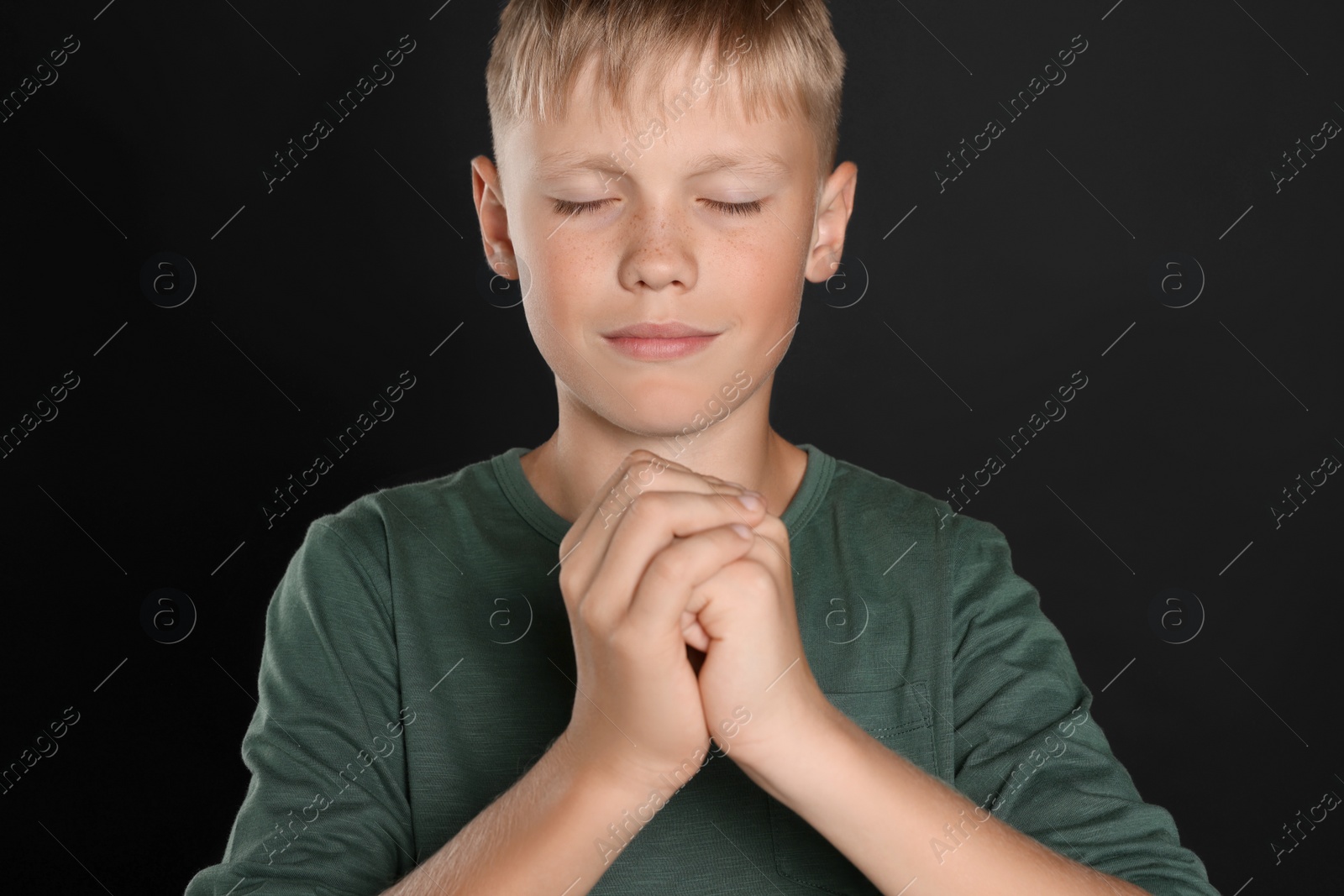 Photo of Boy with clasped hands praying on black background