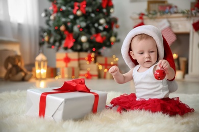 Photo of Cute baby in Santa hat playing with jingle bell at home. Christmas celebration