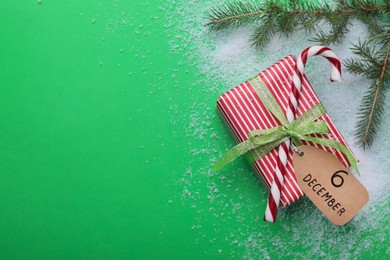 Photo of Gift box, paper tag with date 6th of December, fir tree branch and space for text on green background, flat lay. Saint Nicholas Day