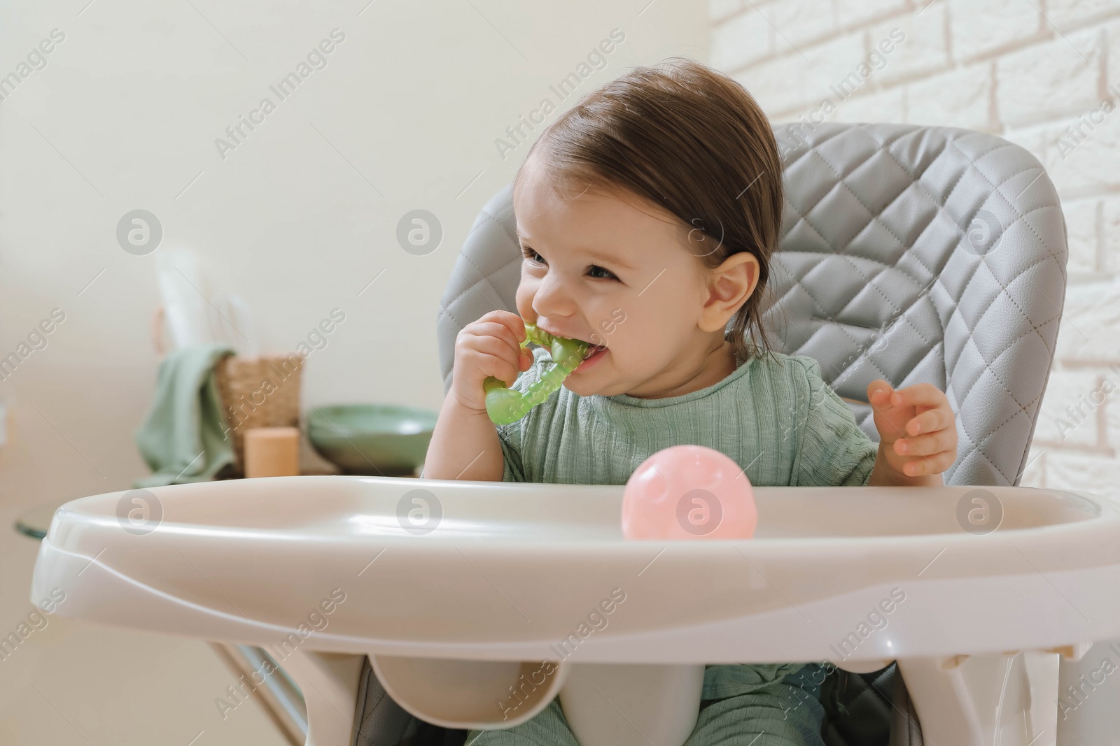 Photo of Cute little baby nibbling teether in high chair indoors