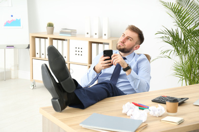 Lazy office employee with mobile phone at workplace