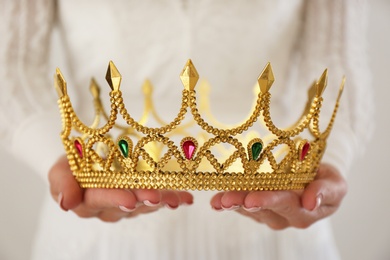 Photo of Woman holding beautiful crown with gems on light background, closeup. Fantasy medieval period