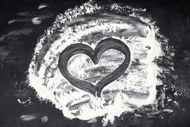 Drawing of heart on flour scattered over black table, top view